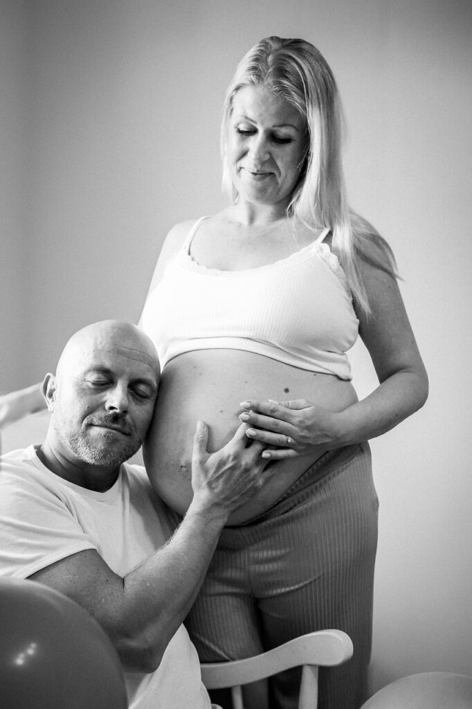 Dasselbe Bild in Schwarzweiß: Der werdende Papa beim Babybauchshooting zuhause. Entspannt und liebevoll dabei.